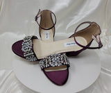 a pair of eggplant purple block heel bridal shoes with an ankle strap and a pearl and crystal design on the front strap of the shoes