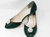 A pair of hunter green satin kitten heels with a peep toe and designed with a crystal design on the front of the shoes