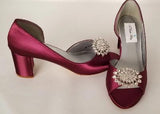 A pair of burgundy shoes with a low block heel and a peep toe front with a crystal design on the front of the shoes