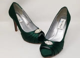 A pair of high heeled hunter green satin shoes with a peep toe and a hidden platform at the front of the shoes and a crystal design on the front of the shoes