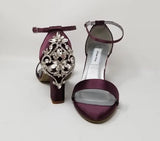 A pair of eggplant purple block heel shoes with an ankle strap and a crystal design on the front toe strap of the shoes and a crystal design on the heel of the shoes