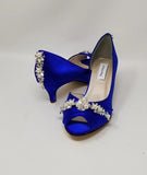 A pair of royal blue satin kitten heel shoes with a peep toe and a crystal and pearl design on the front and the back heel of the shoes