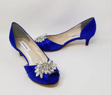 A pair of royal blue satin kitten heels with a peep toe and designed with a crystal design on the front of the shoes