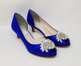 A pair of royal blue satin kitten heels with a peep toe and designed with a crystal design on the front of the shoes