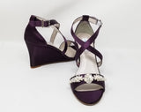 A pair of eggplant purple wedding shoes with high wedge and straps across the front of the foot designed with a pearl and crystal design on the front toe strap of the shoes