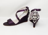 A pair of eggplant purple wedding shoes with high wedge and straps across the front of the foot designed with a crystal design on the front toe strap of the shoes and a crystal design on the back heel of the shoes