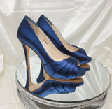A pair of high heeled navy blue satin shoes with a peep toe and a hidden platform at the front of the shoes
