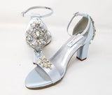 A pair of baby blue block heel shoes with an ankle strap and a crystal design on the front toe strap of the shoes and a crystal design on the heel of the shoes