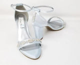 A pair of baby blue block heel shoes with an ankle strap and a crystal design on the front toe strap of the shoes and a crystal design on the heel of the shoes