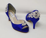 A pair of royal blue satin medium height heel bridal shoes with a peep toe and designed with a crystal design on the front of the shoes and a crystal design on the back heel of the shoes
