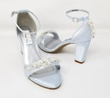 A pair of baby blue block heel shoes with an ankle strap and a pearl and crystal design on the front toe strap of the shoes and a pearl and crystal design on the heel of the shoes