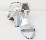 A pair of baby blue block heel shoes with an ankle strap and a crystal design on the front toe strap of the shoes and a crystal design on the heel of the shoes