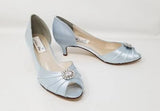A pair of baby blue satin kitten heel shoes with a peep toe with a small crystal design on the front of the shoes