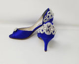A pair of royal blue satin medium height heel bridal shoes with a peep toe and designed with a crystal design on the front of the shoes and a crystal design on the back heel of the shoes