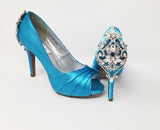 A pair of high heeled turquoise satin shoes with a peep toe and a hidden platform at the front of the shoes and a crystal design on the back heel of the shoes