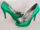A pair of high heeled emerald green satin shoes with a peep toe and a hidden platform at the front of the shoes and a crystal and pearl design on the front of the shoes