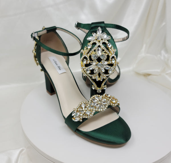 A pair of hunter green block heel shoes with an ankle strap and a gold crystal design on the front toe strap of the shoes and a gold crystal design on the heel of the shoes