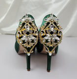 A pair of high heeled hunter green satin shoes with a peep toe and a hidden platform at the front of the shoes and a gold crystal design on the back heel of the shoes