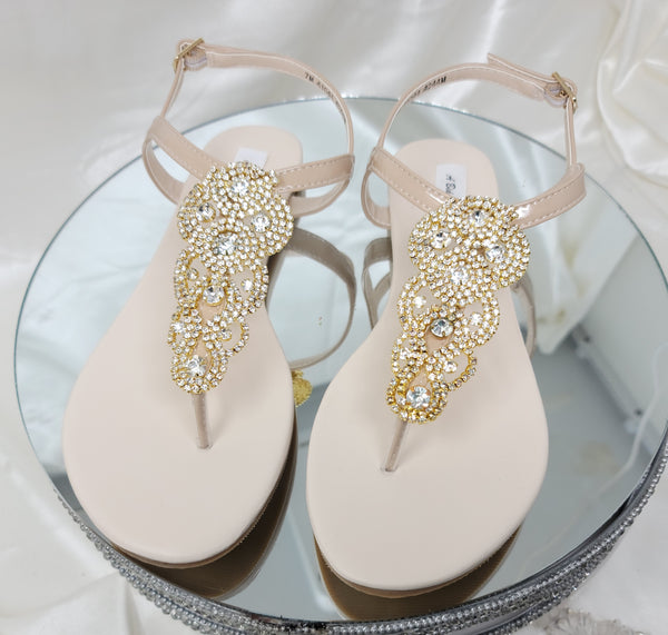 a pair of flat heel ivory bridal sandals with gold crystals on the straps of the sandals