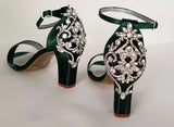 A pair of hunter green block heel shoes with an ankle strap and a crystal design on the front toe strap of the shoes and a crystal design on the heel of the shoes