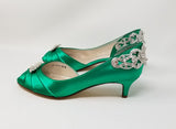 A pair of emerald green satin kitten heels with a peep toe and designed with a crystal design on the front of the shoes and a large crystal design on the back heel of the shoes
