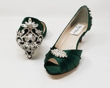 A pair of hunter green satin kitten heels with a peep toe and designed with a crystal design on the front of the shoes and a large crystal design on the back heel of the shoes