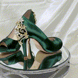 A pair of high heeled hunter green satin shoes with a peep toe and a hidden platform at the front of the shoes and a gold crystal design on the back heel of the shoes
