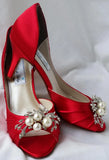 A pair of red satin medium height heel shoes with a peep toe and designed with a pearl and crystal design on the front of the shoes