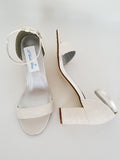 A pair of ivory lace covered low block heel shoes with an ankle strap