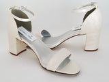 A pair of ivory lace covered low block heel shoes with an ankle strap