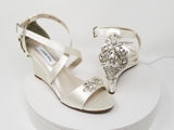 A pair of ivory wedding shoes with high wedge and straps across the front of the foot designed with a crystal design on the front toe strap and a crystal design on the back heel of the shoes