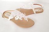 a pair of flat heel ivory bridal sandals with lace and pearls on the straps of the sandals