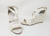 A pair of ivory wedding shoes with high wedge and straps across the front of the foot designed with a lace design on the front toe strap and a lace design on the back heel of the shoes