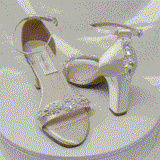 A pair of ivory block heel shoes with an ankle strap and a pearl and crystal design on the front toe strap of the shoes and a pearl and crystal design on the heel of the shoes