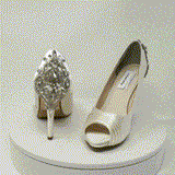 A pair of high heeled ivory satin shoes with a peep toe and a hidden platform at the front of the shoes and a crystal design on the back heel of the shoes