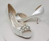 A pair of ivory satin medium height heel shoes with a peep toe and designed with a crystal vine design on the front and side of the shoes