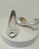 A pair of ivory satin kitten heel shoes with a peep toe with a small crystal design on the front of the shoes