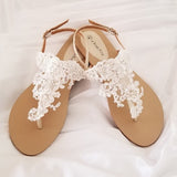 a pair of flat heel ivory bridal sandals with lace and pearls on the straps of the sandals