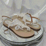 a pair of flat heel ivory bridal sandals with lace and pearls on the straps of the sandals