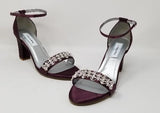 A pair of eggplant purple block heel shoes with an ankle strap and a crystal design on the front toe strap of the shoes
