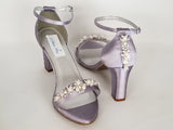 A pair of lilac purple block heel shoes with an ankle strap and a crystal and pearl design on the front toe strap of the shoes and a crystal and pearl design on the heel of the shoes