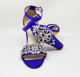 A pair of purple high block heel shoes with an ankle strap and a crystal and pearl design on the front toe strap of the shoes and a large crystal design on the back heel of the shoes