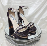 A pair of eggplant purple high block heel platform shoes with an ankle strap and a crystal design on the front toe strap of the shoes and a crystal design on the ankle strap of the shoes