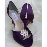 A pair of eggplant purple satin medium height heel bridal shoes with a peep toe and designed with a crystal design on the front of the shoes and a crystal teardrop design on the back heel of the shoes