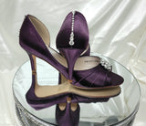 A pair of eggplant purple satin medium height heel bridal shoes with a peep toe and designed with a crystal design on the front of the shoes and a crystal teardrop design on the back heel of the shoes