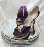 A pair of eggplant purple satin medium height heel bridal shoes with a peep toe and designed with a crystal design on the front of the shoes and a crystal teardrop design on the back heel of the shoes