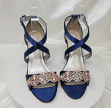 A pair of navy blue wedding shoes with high wedge and straps across the front of the foot designed with a rose gold crystal design on the front toe strap of the shoes