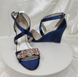 A pair of navy blue wedding shoes with high wedge and straps across the front of the foot designed with a rose gold crystal design on the front toe strap of the shoes