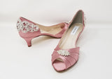 A pair of dusty rose satin kitten heels with a peep toe and designed with a crystal design on the front of the shoes and a crystal design on the back heel of the shoes