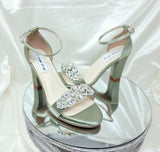 A pair of sage green block heel shoes with an ankle strap and a crystal design on the front toe strap